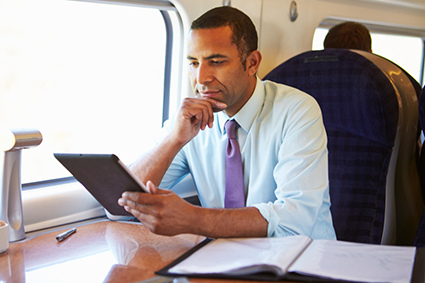 Businessman Commuting On Train Using Digital Tablet alternate text for this image