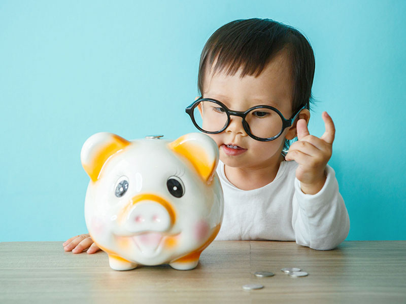 Fillette déposant une pièce de monnaie dans une tirelire.