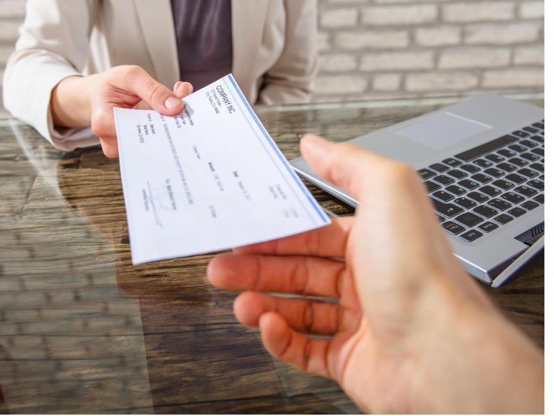 Un homme assis à une table tendant un chèque de paie à une personne en face de lui.