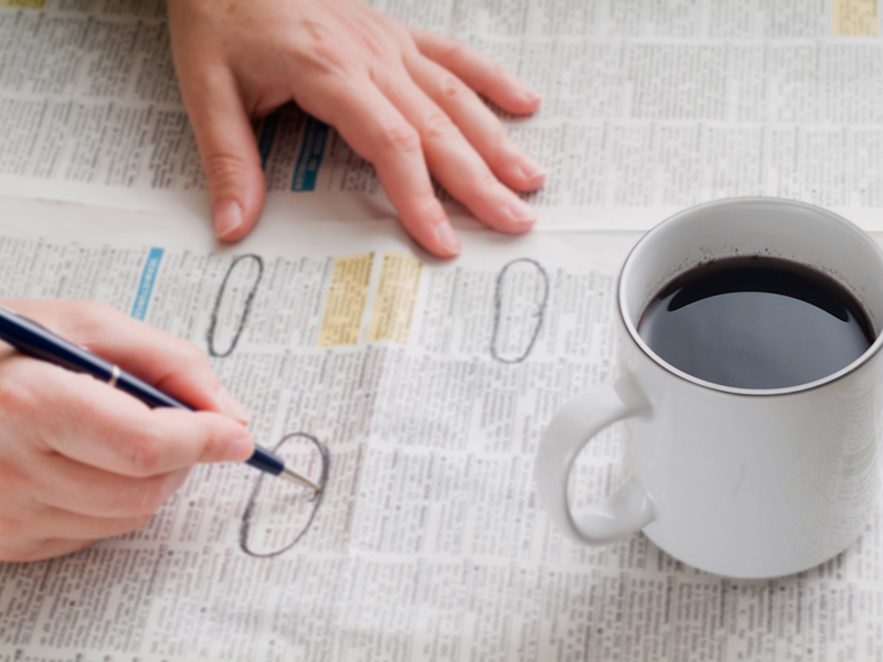 Une personne assise à une table devant un journal et un café qui entoure les petites annonces.