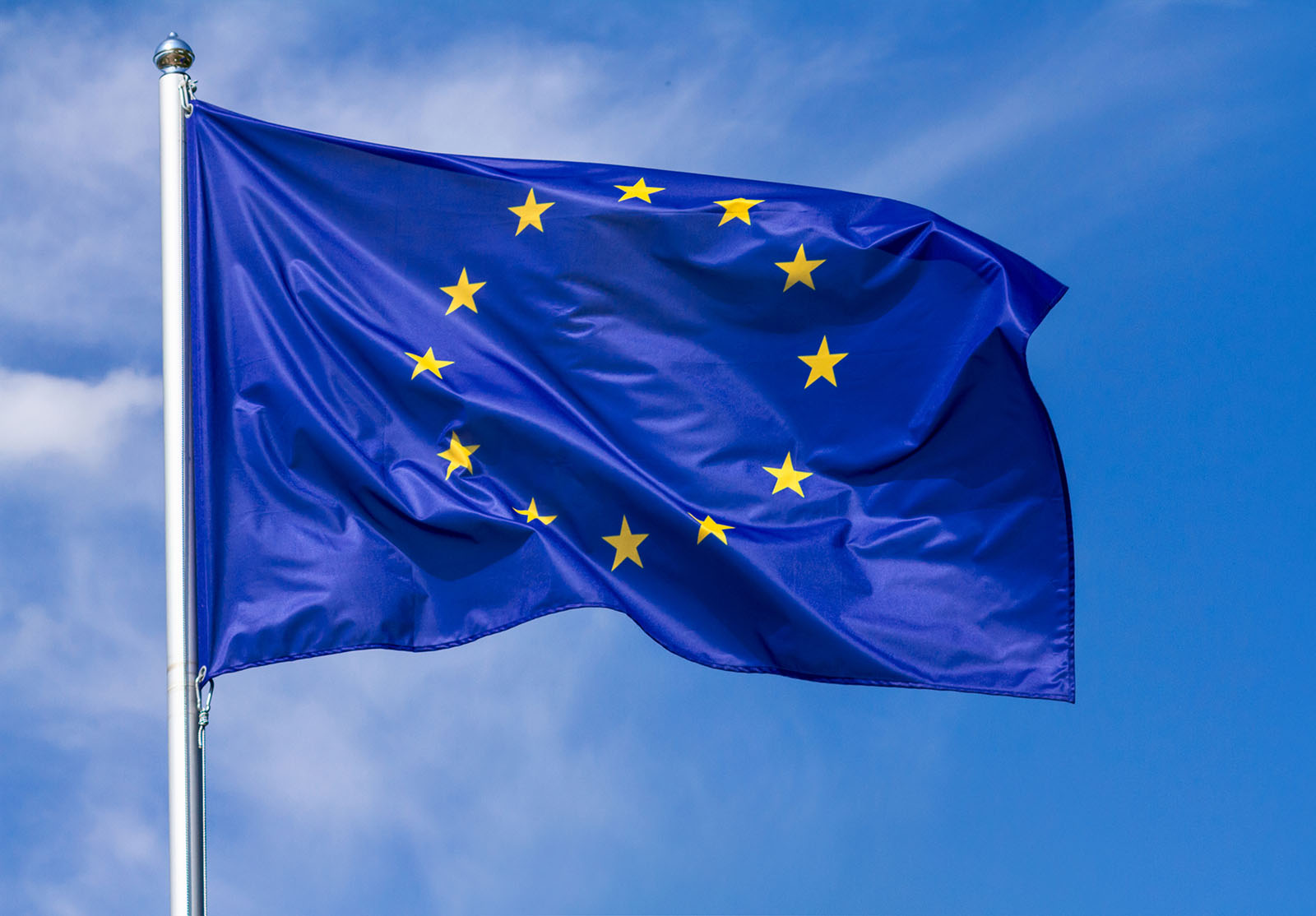 Drapeau de l'Union européenne flottant au vent sur un mât, sur fond de ciel nuageux par une journée ensoleillée, bannière, gros plan