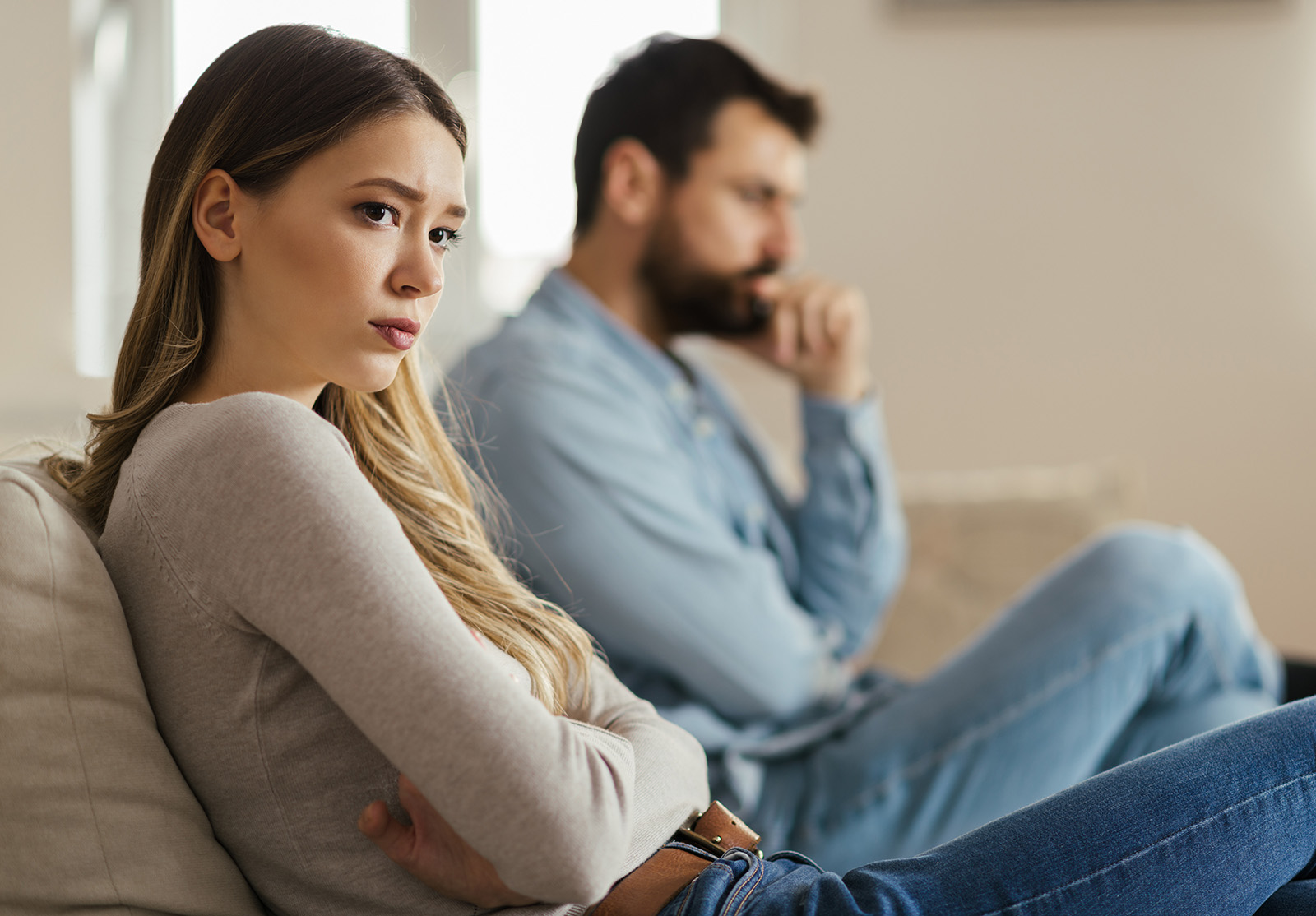 Jeune femme inquiète, assise sur le canapé à la maison et ignorant son petit ami qui est assis à côté d'elle.