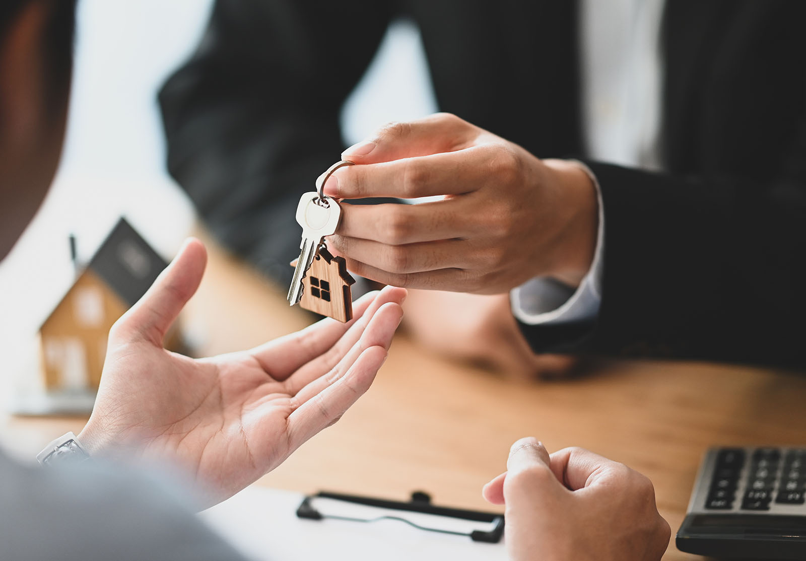 Plan recadré d'un courtier immobilier remettant une clé de propriété à son client pendant qu'il rédige/signe un contrat sur un bureau moderne en bois. Concept d'accord de prêt, de dette, de crédit, d'achat ou de vente.