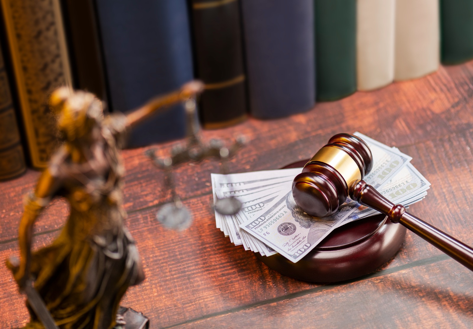 Un marteau de justice posé sur son socle, mais sur celui-ci il y a une liasse de billets américains. À côté, on voit une statue de la Justice en flou.