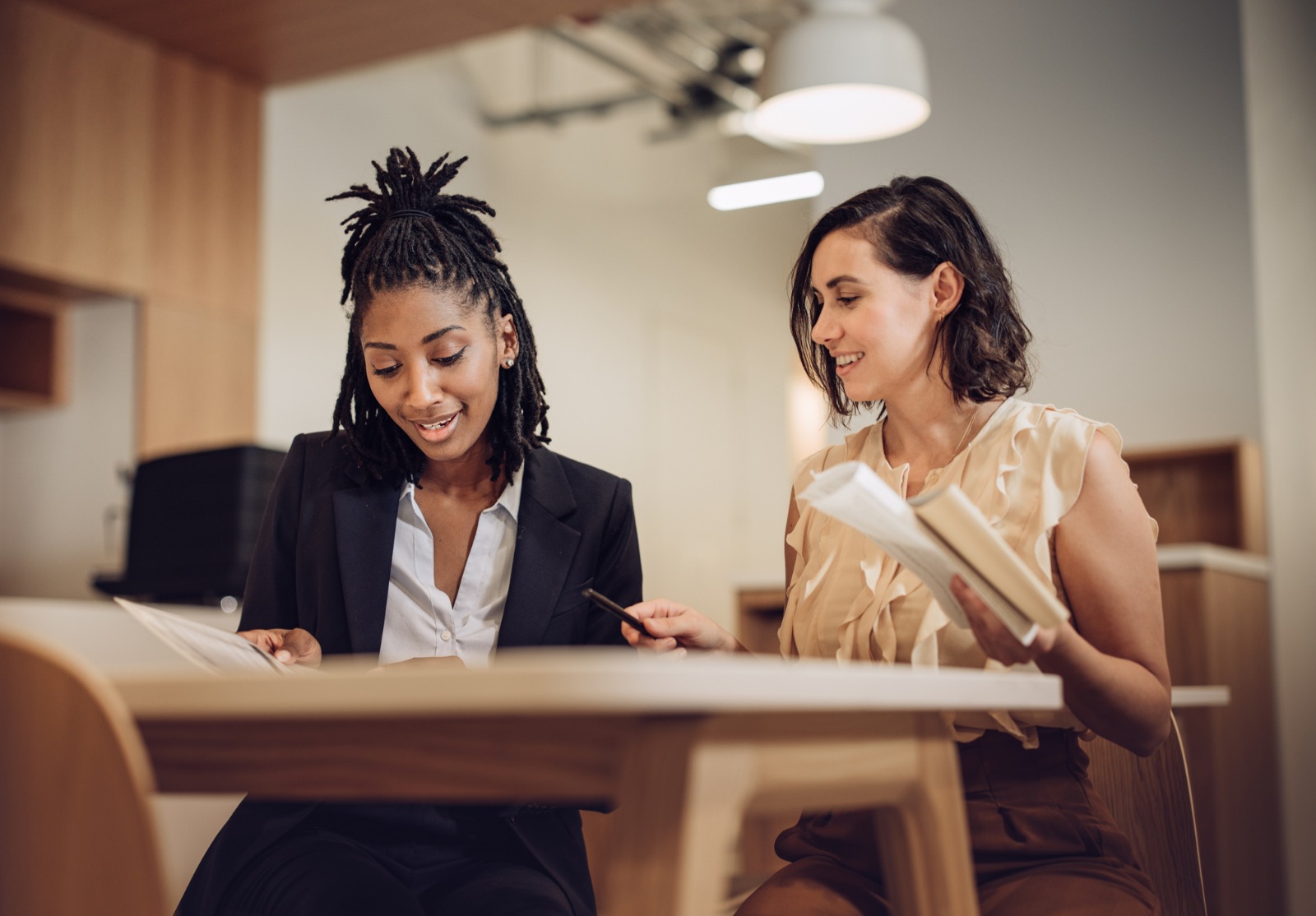 Deux femmes assises à une table et semblant apprendre quelque chose.