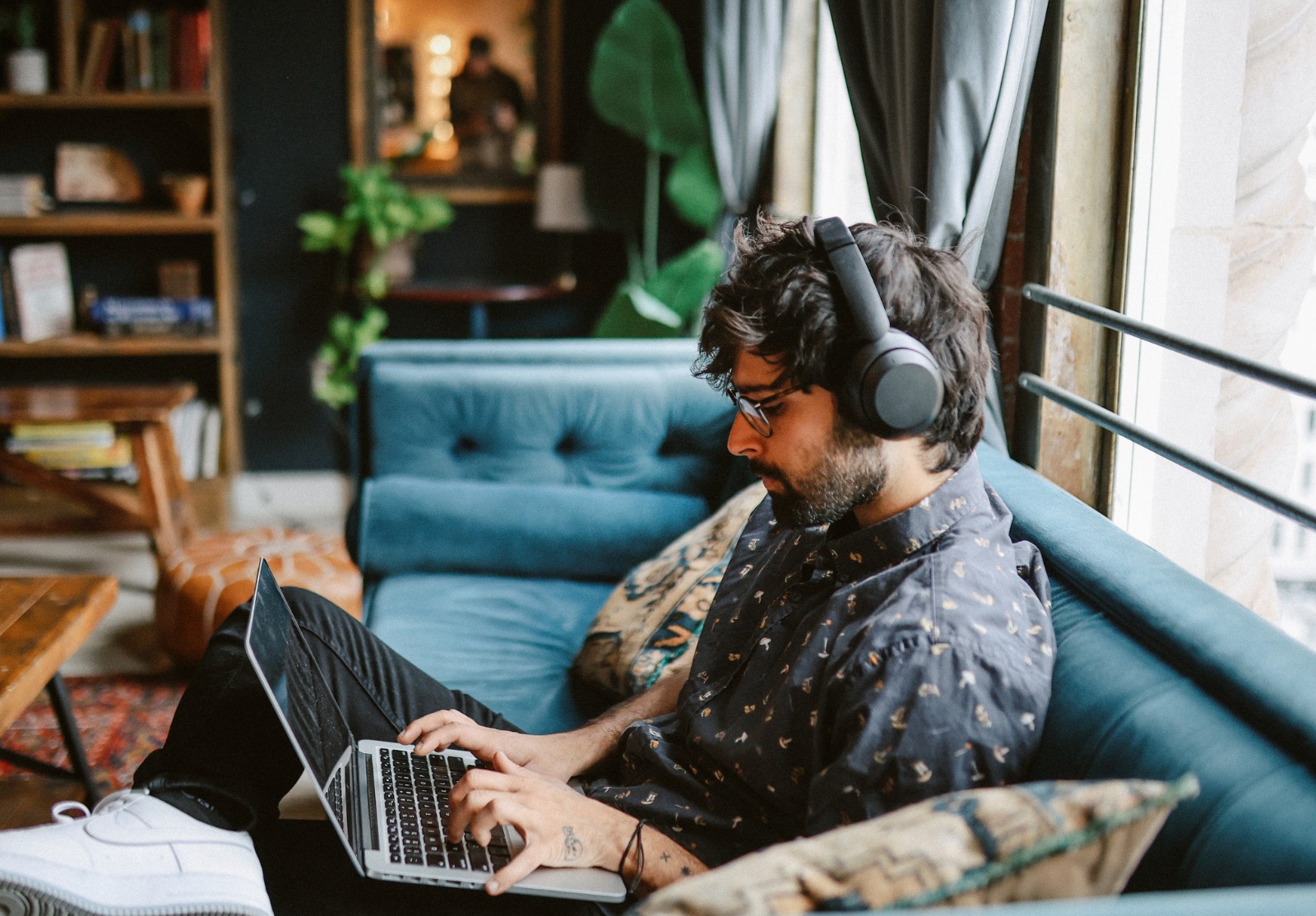 Un homme avec des écouteurs, assis sur son canapé, travaillant sur son ordinateur. Travail à domicile dans le centre-ville de Los Angeles.