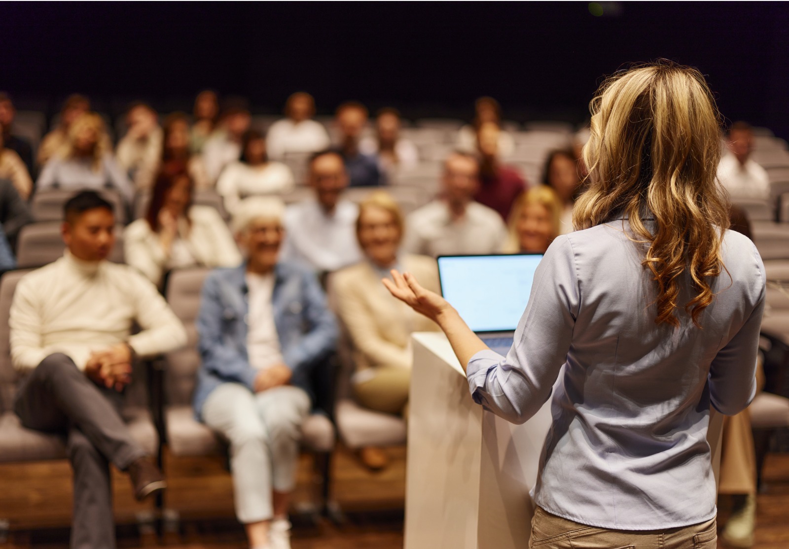 Vue arrière d’une conférencière prononçant un discours devant des personnes au centre des congrès.