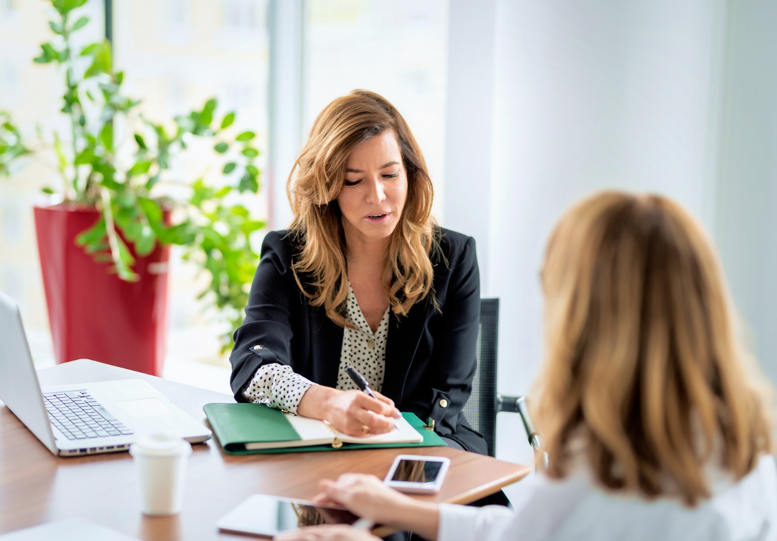 Femme d'affaire à un bureau, écrivant sur un document alors qu'elle parle avec une autre femme.