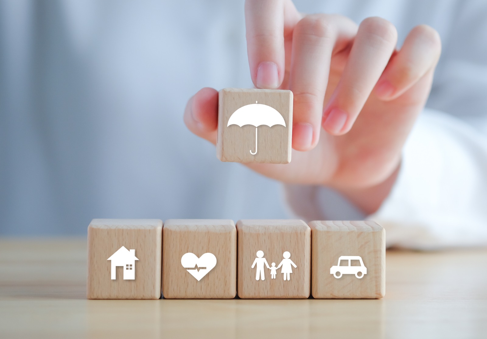 Concept d’assurance. Protection contre une éventuelle éventualité. Icône de parapluie tenant la main et icône maison, voiture, famille et santé sur bloc de bois pour le concept de vie d’assurance.