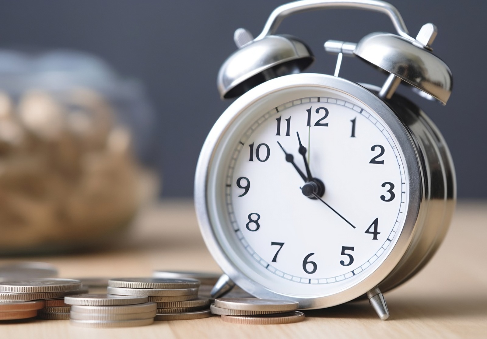 À côté d’une horloge se trouve une pile de pièces de monnaie, symbolisant l’expression « le temps, c’est de l’argent ».