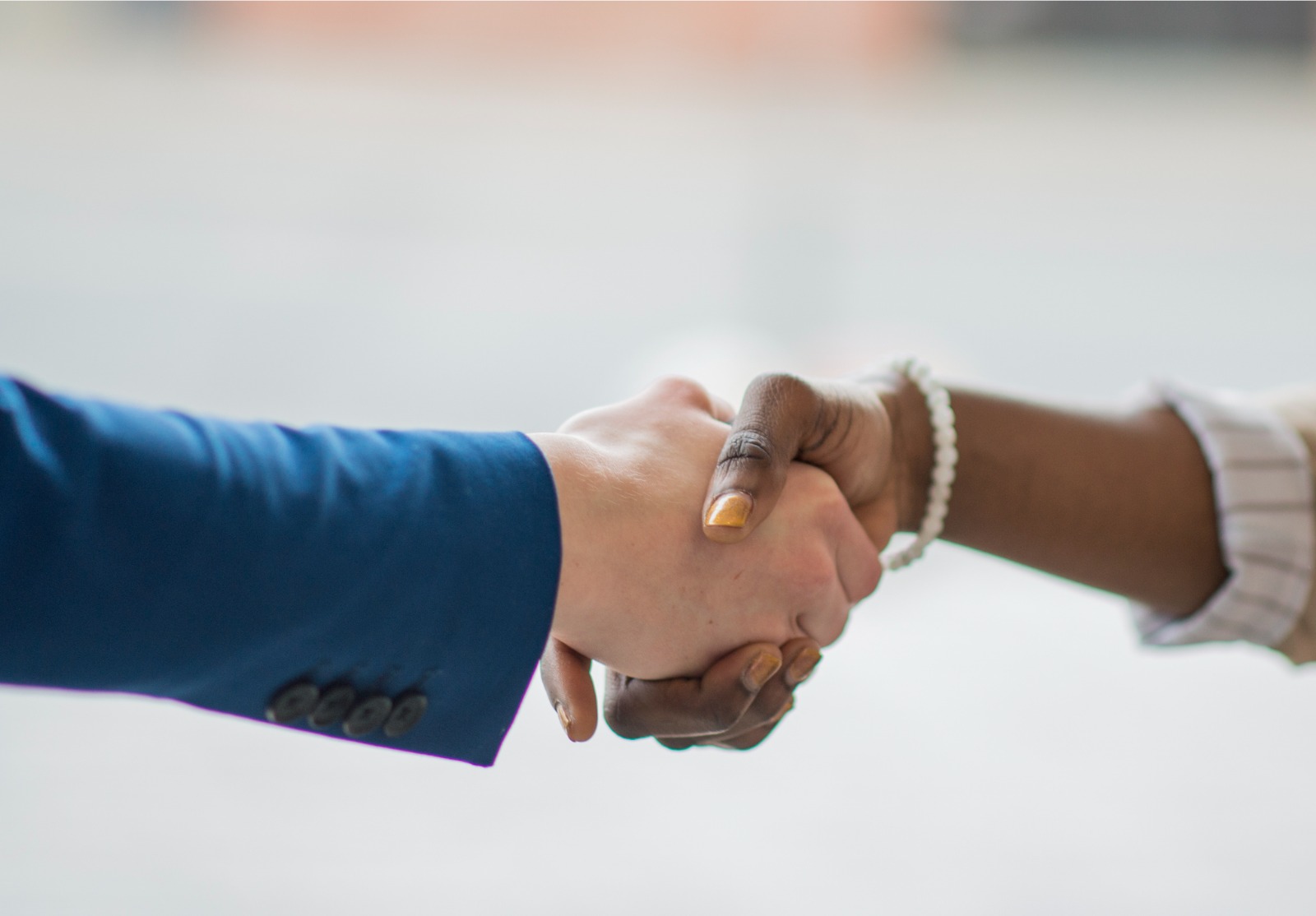 Deux mains qui se serrent, l'une appartient à une femme noire, l'autre à un homme blanc.