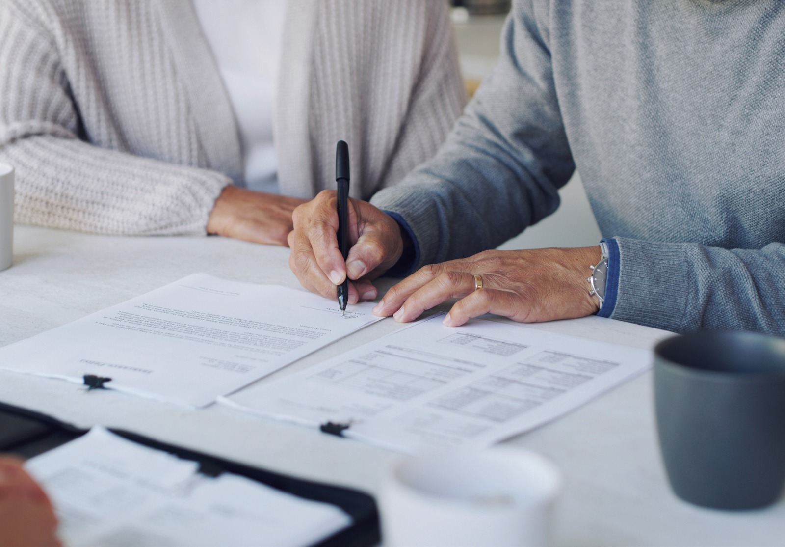 Un couple assis à une table face à quelqu'un. L'homme signe un document.