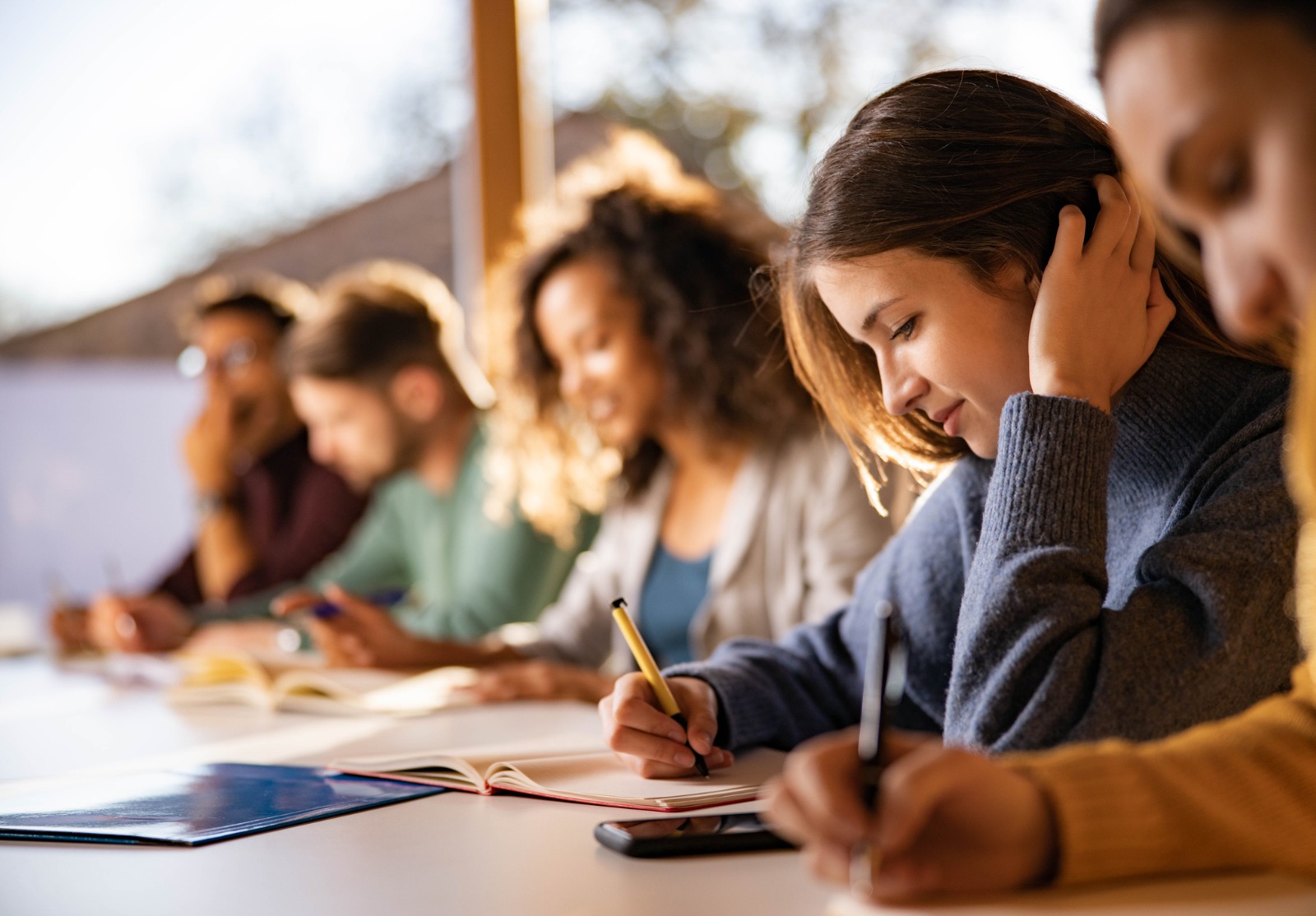 Une femme dans une salle de cours avec d'autres étudiants. Elle écrit dans un livre.