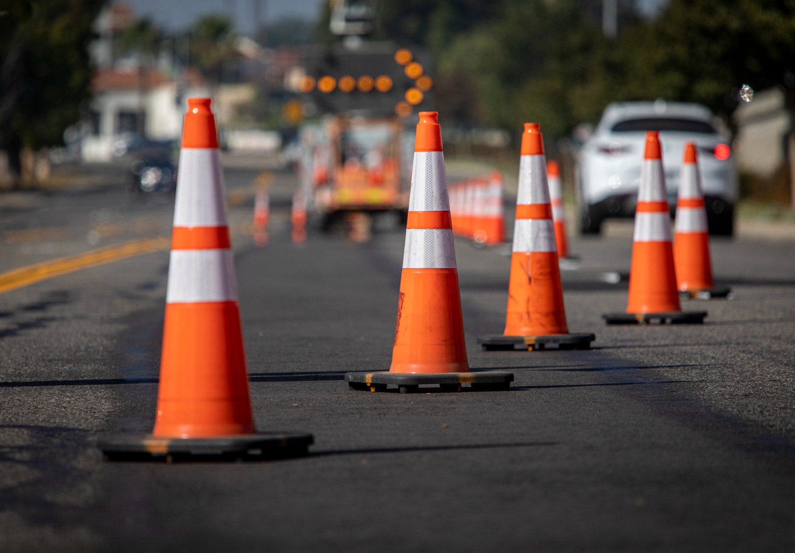 Cônes de signalisation sur la route avec flèche électronique pointant vers la droite pour dévier la circulation et voiture blanche en distance.