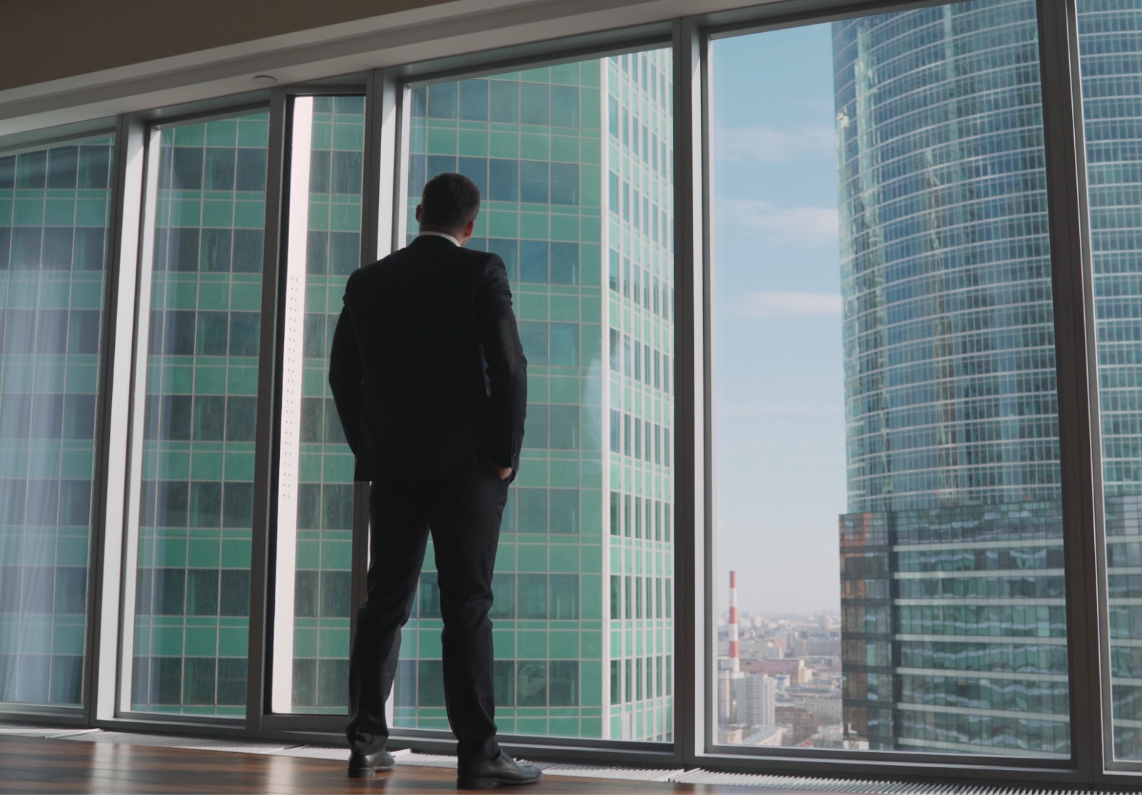 Jeune homme d’affaires prospère debout devant les fenêtres, regardant au loin de la ville. L’homme qui réussit se tient dans le néoboksreb. Un homme d’affaires se tient devant une fenêtre et la regarde.