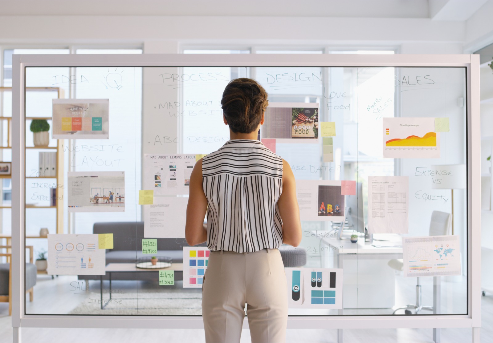 Une femme devant un tableau transparent plein d'images et d'écriture.