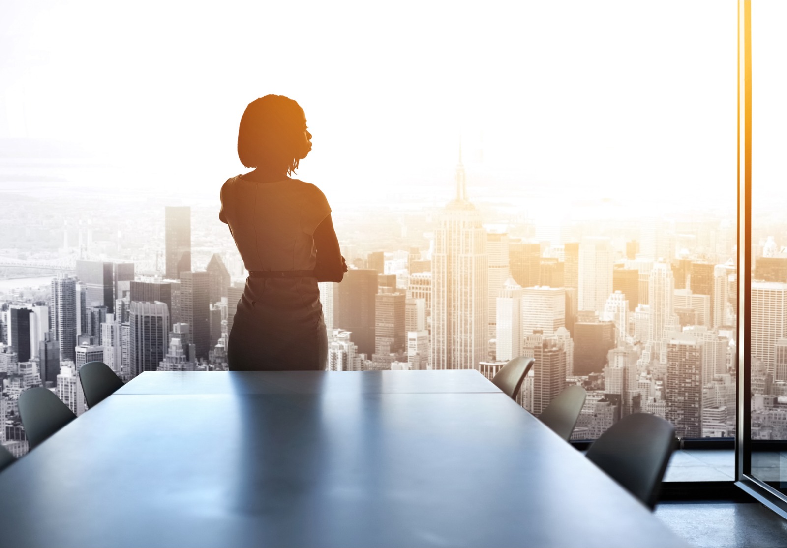 Une femme d'affaire devant une fenêtre qui regarde la ville depuis un bureau dans un building.
