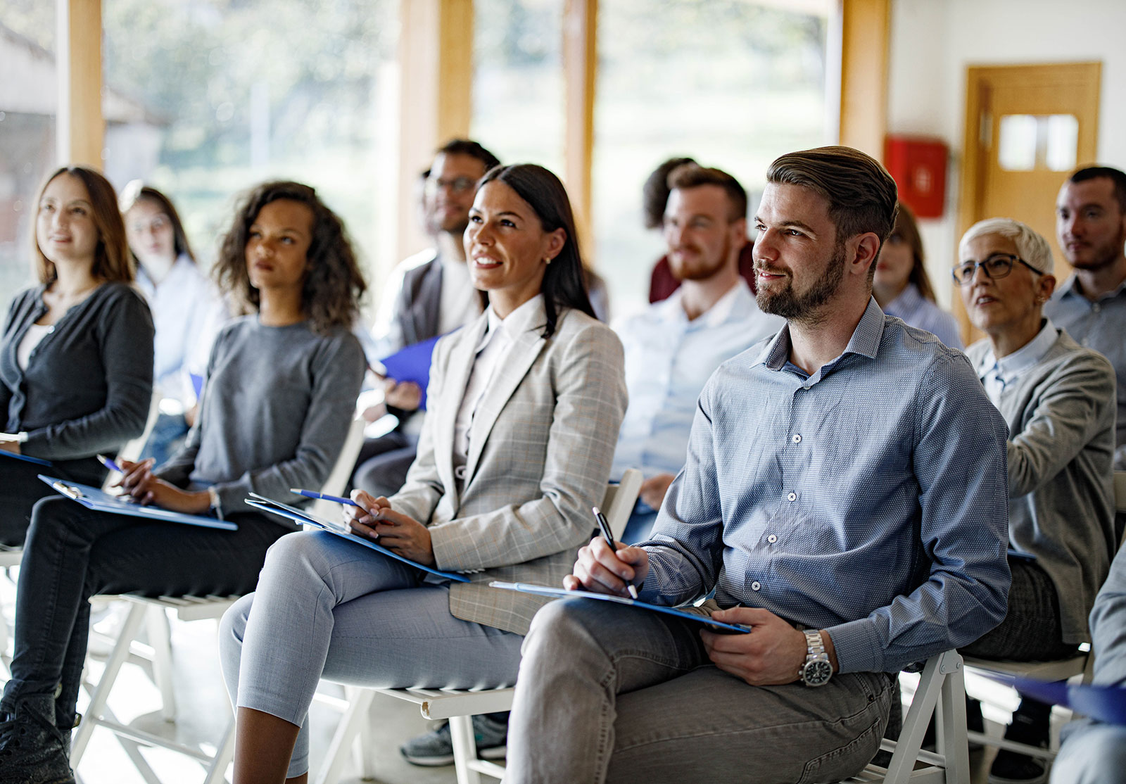 Des personnes assise dans une salle avec un bloc et des stylos qui écoutent attentivement quelqu'un en face d'eux.