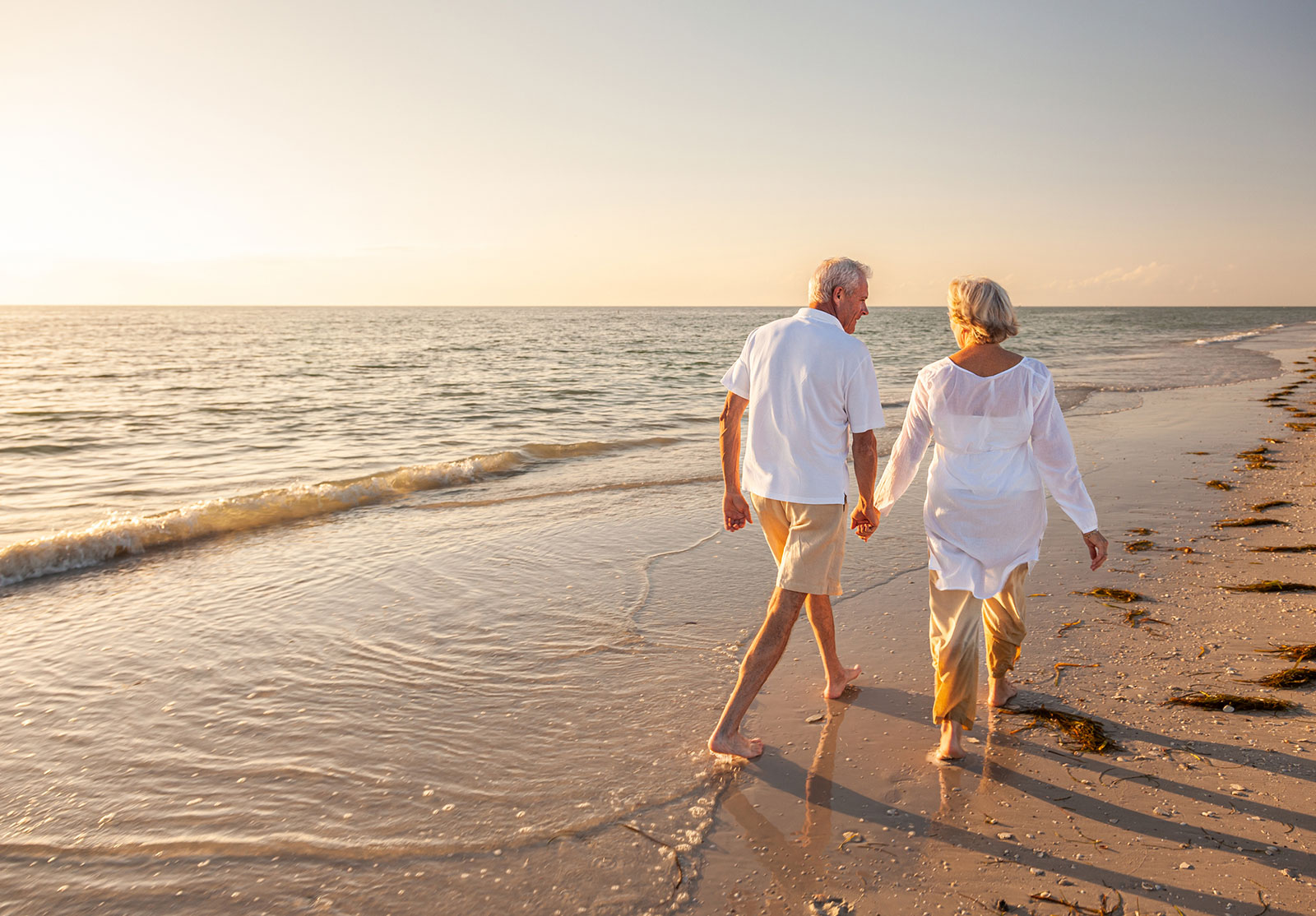 Un homme et une femme d'un certain âge qui marchent sur une plage au bord de la mer en se donnant la main.