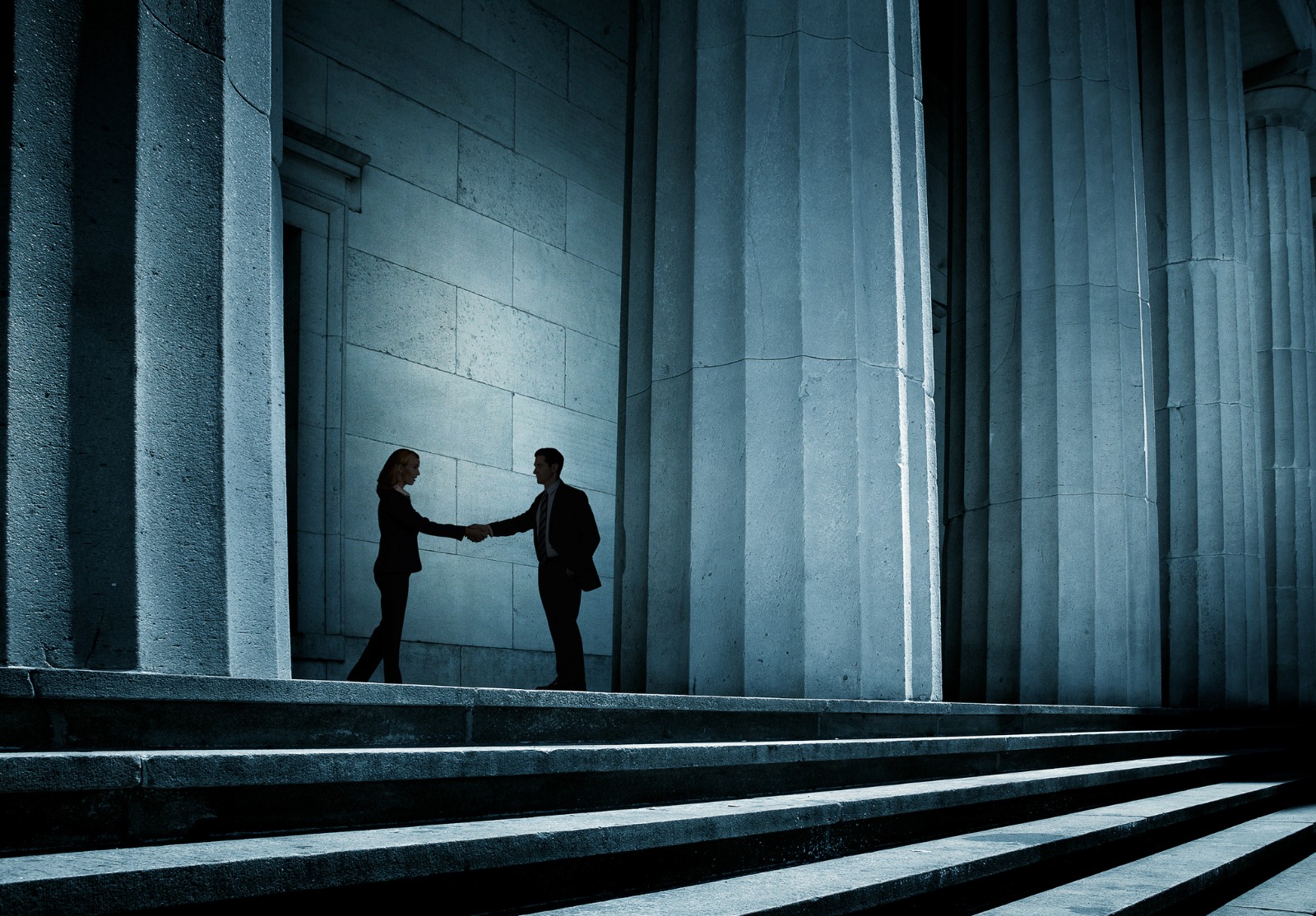 Un homme et une femme se serrent la main dans l’ombre.