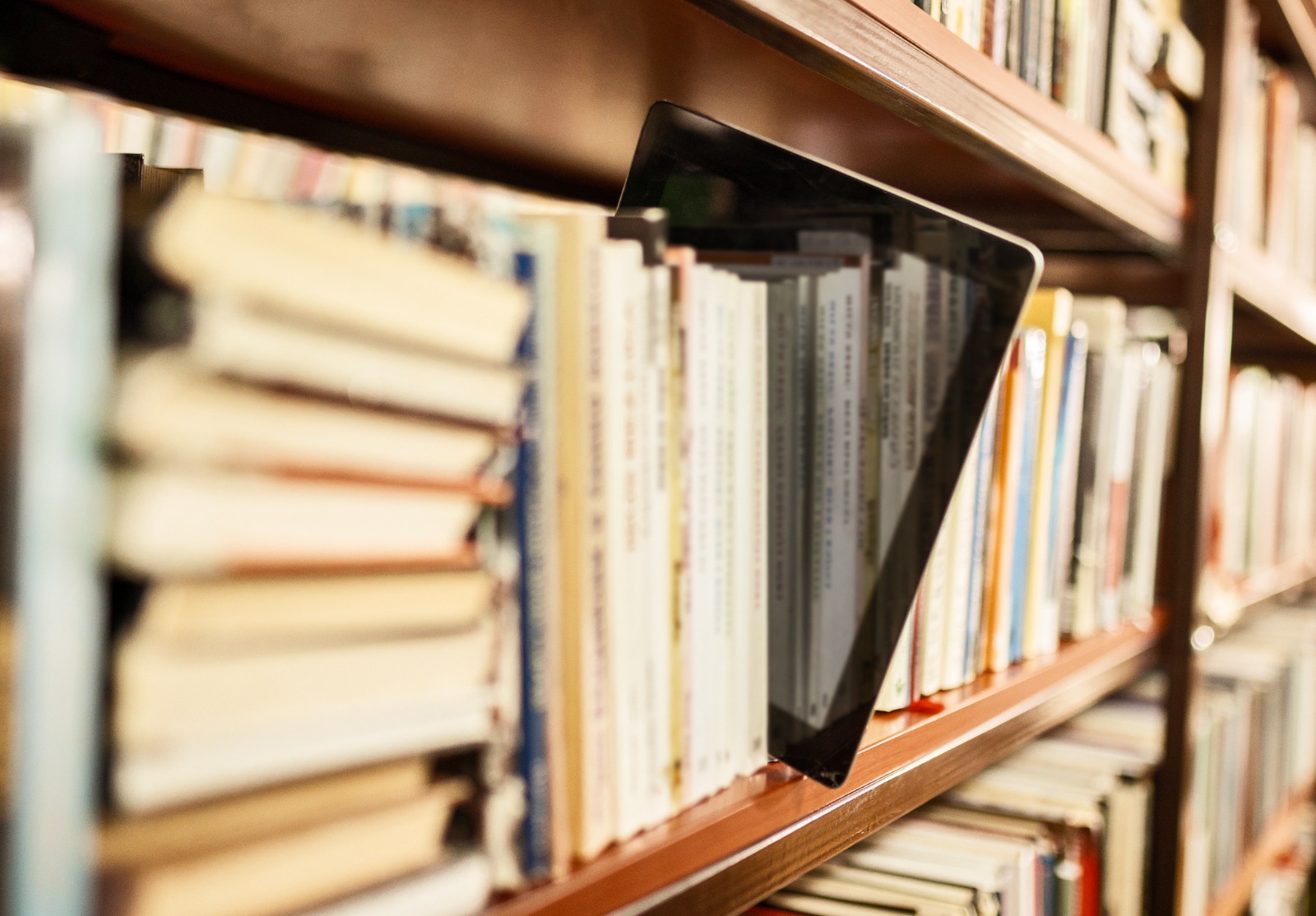 Vue de la tablette numérique sur l’étagère d'une bibliothèque entourée de livre.