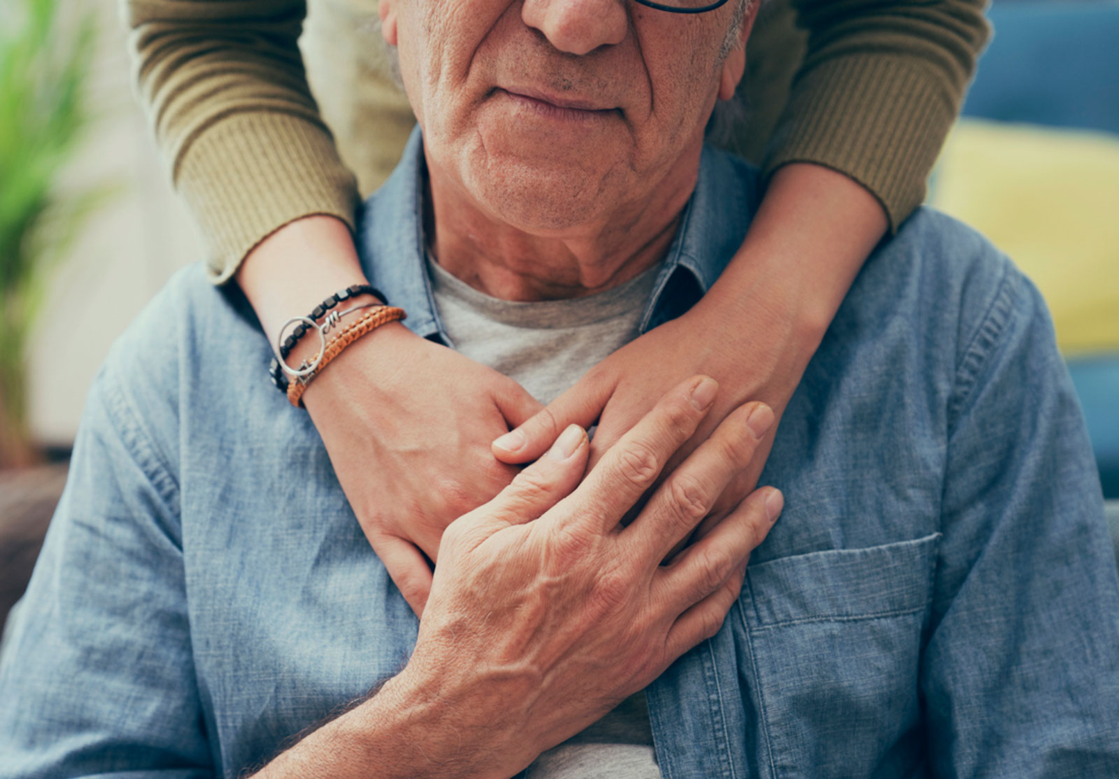 Une jeune femme placée derrière une personne âgée avec les bras posés sur ses épaules, dans un geste très tendre. L'homme âgé tient une des mains de la jeune femme.