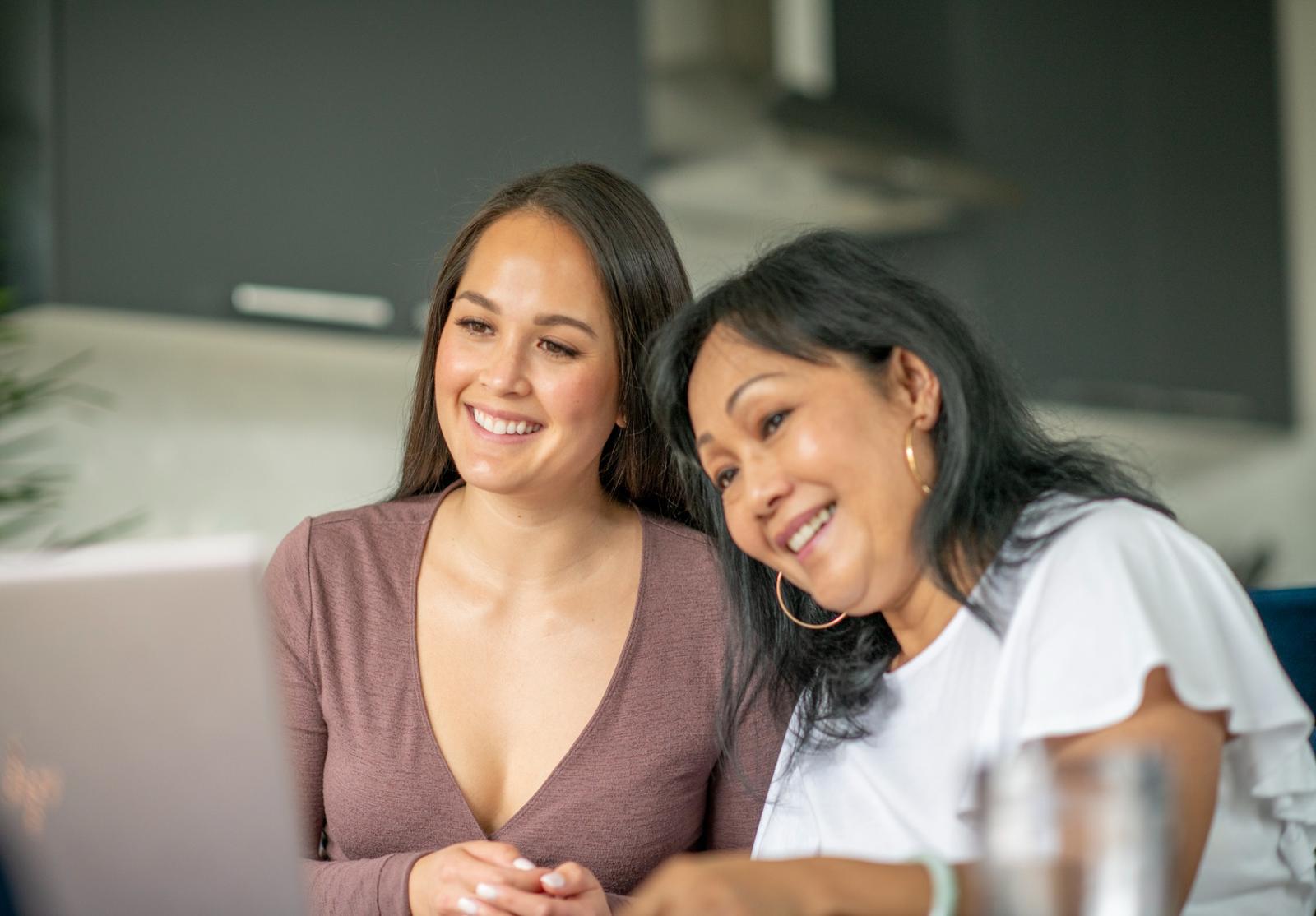 Deux femmes souriantes regardent un écran d’ordinateur ensemble, probablement lors d’une séance de travail ou de formation en ligne.