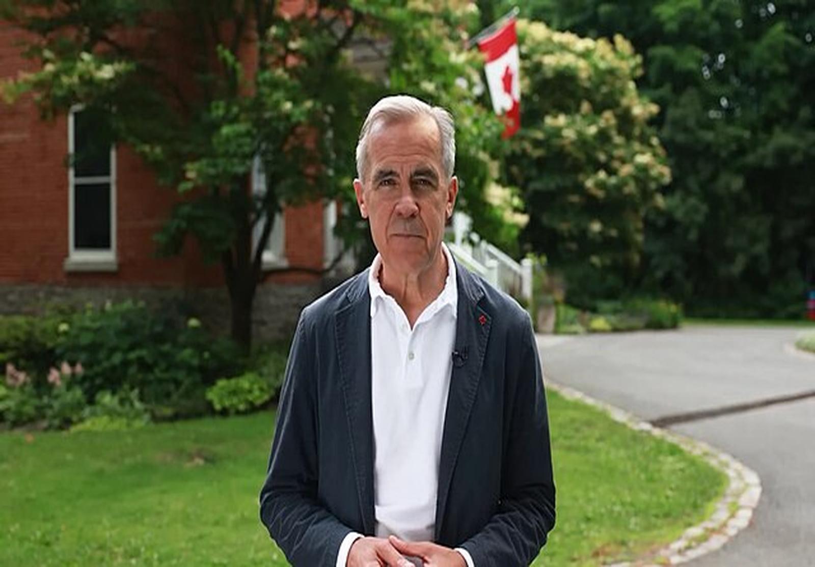 Portrait de Mark Carney à l’extérieur, vêtu d’une veste sombre et d’une chemise blanche. En arrière-plan, un drapeau canadien flotte devant un bâtiment en brique rouge entouré de verdure. L’image reflète un message institutionnel ou patriotique.