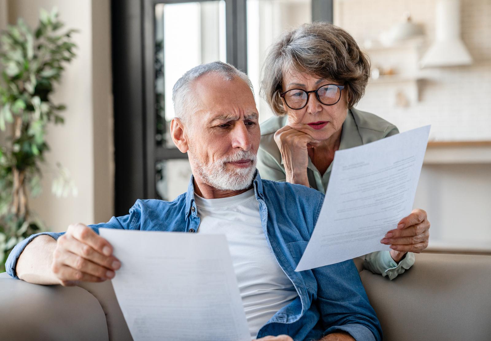 Couple senior assis dans le salon, regardant sérieusement des documents importants.