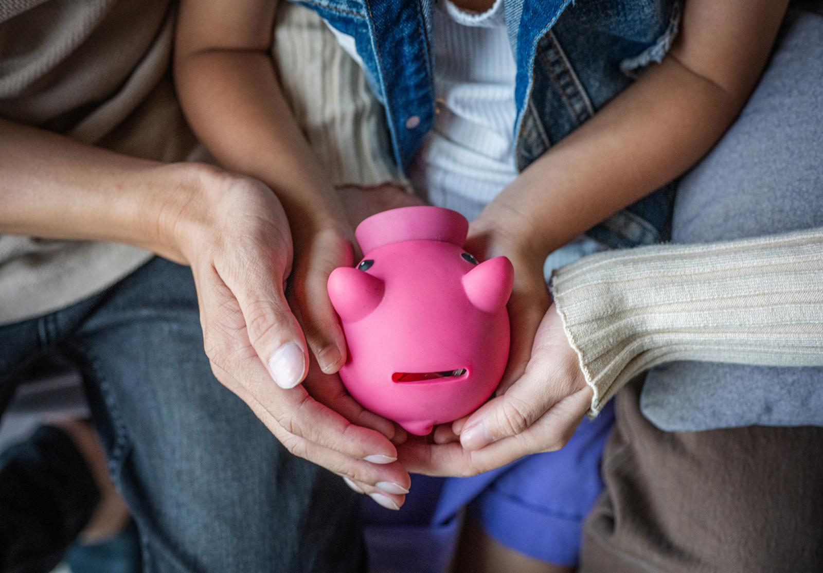 Mains de parents et d’enfant tenant une tirelire rose en forme de cochon.