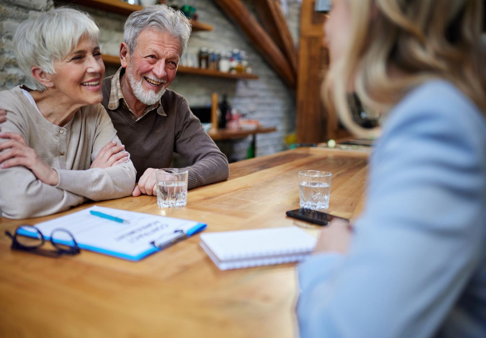 Couple de retraités souriants discutant avec une conseillère autour d'une table.