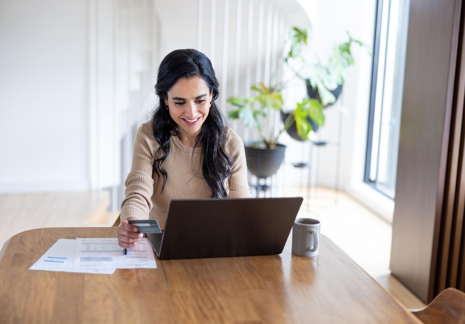 Femme souriante effectuant une transaction en ligne à domicile avec une carte bancaire.