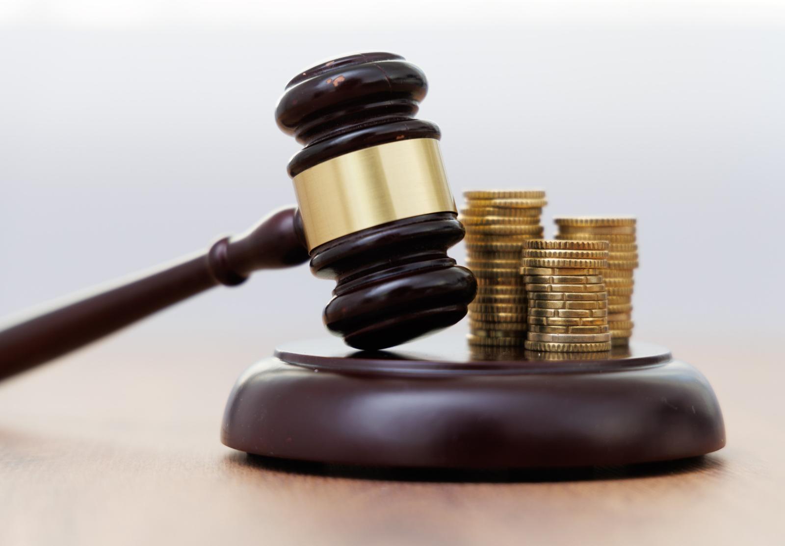 Marteau de juge posé devant des piles de pièces de monnaie dorées, illustrant la justice financière.